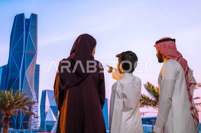 الاشارة الى الأبراج الاقتصادية والمنشأت المعمارية، أماكن سياحية مشهورة, النمو والتطورالعمراني في الأحياء الجديده في الرياض, صورة من الخلف لعائلة عربية خليجية تقف أمام مركز الملك عبدالله المالي ( كافد ) في السعودية، الفن الهندسي للابراج وناطحات السحاب
