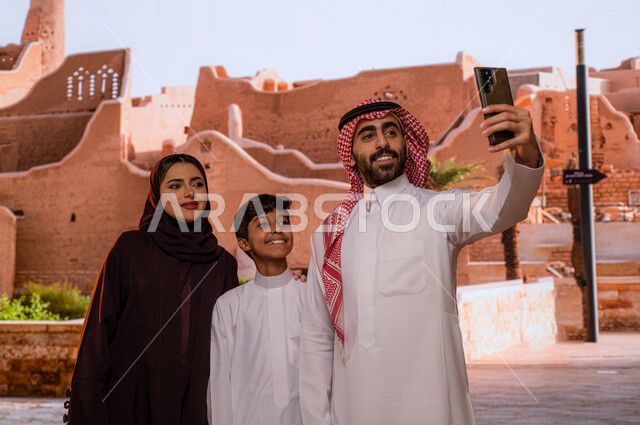 معلم ومنتزه  تاريخي تراثي على الطراز الشعبي القديم, الاستمتاع بالآثار و المباني الطينيه في حي البجيري في مدينة الدرعية في الرياض ، مركز ثقافي وطني سياحي, صورة مقربة لعائلة عربية خليجية سعودية تقف امام قصر سلوى وتلتقط  صور السيلفي التذكارية عبر الجوال