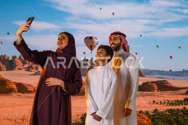 انشطه وفعاليات ترفيهيه ،الطيران في بالون الهواء الساخن في محافظة العلا, وجهة عائلية سياحية طبيعيه, صورة مقربة من الخلف لعائلة عربيه خليجية سعودية تلتقط صور السيلفي التذكارية عبر الجوال، المناطيد في سماء المملكة العربية السعودية، معالم أثرية تاريخية قديمة