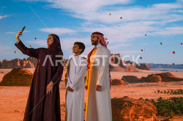 الطيران في بالون الهواء الساخن في محافظة العلا, وجهة عائلية سياحية طبيعيه, انشطه وفعاليات ترفيهيه ،صورة من الخلف لعائلة عربيه خليجية سعودية تلتقط صور السيلفي التذكارية عبر الجوال، المناطيد في سماء المملكة العربية السعودية، معالم أثرية تاريخية قديمة 
