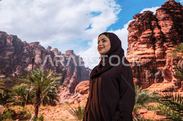 Cultivation of palm trees and green plants in tourist places in Al-Ula Governorate in Saudi Arabia, an archaeological site in UNESCO, gestures indicating joy and happiness, a close-up of a smiling Saudi Arab woman wearing the Gulf abaya visiting the most 