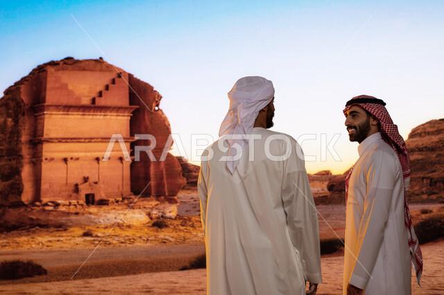 قصر الفريد في محافظة العلا في السعودية ,صورة من الخلف لسائح عربي اماراتي خليجي يرتدي الكندورة والعمامة البيضاء مع رجل سعودي يتبادلان الاحاديث, الاستمتاع بالمناظر الطبيعية الصحراوية التاريخية الاثرية العريقة القديمة, انشطه ترفيهيه سياحية