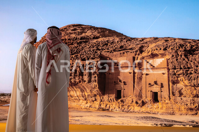  السياحة في السعودية، صورة من الخلف لرجل سعودي مع رجل اماراتي يرتدي العمامة والكندورة الامارتية يستمتع بالمناظر الطبيعيه التاريخية الأثرية القديمة, النظر إلى التشكيلات و التكوينات الصخرية في مدائن صالح في محافظة العلا، قدوم السياح من شتى أنحاء العالم