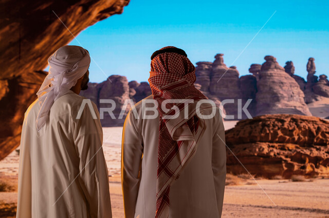 المرتفعات و القمم الجبلية الصخرية ,السياحة في السعودية، قدوم السياح من شتى أنحاء العالم، الوقوف أمام التشكيلات و التكوينات الصخرية في محافظة العلا ,صورة من الخلف لرجل سعودي مع سائح عربي اماراتي يرتدي العمامة والكندورة يستمتع بالمناظر الطبيعية الاثرية