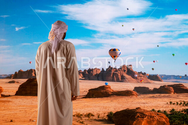 معالم أثرية تاريخية قديمة ،الطيران في بالون الهواء الساخن, التشكيلات و التكوينات الصخرية في محافظة العلا, انشطه ترفيهيه سياحية ،صورة من الخلف لرجل عربي امارتي خليجي يرتدي العمامة والكندورة الاماراتية ينظر إلى المناطيد في سماء السعودية .