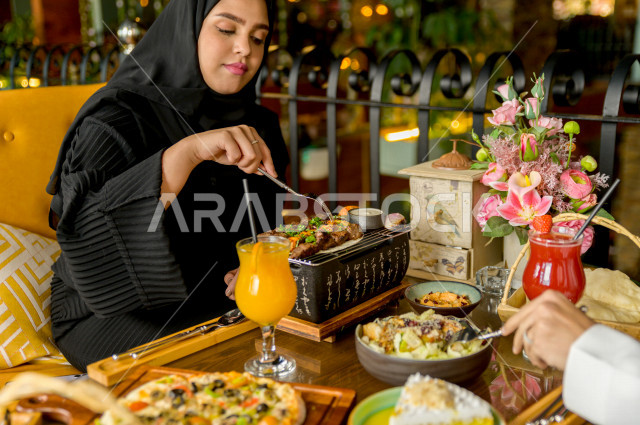 A close-up photo of a Saudi Arabian Gulf woman eating with her husband in the restaurant, spending a wonderful atmosphere in the restaurant, many types of food and dishes on the table, unique and distinctive sessions, restaurants and cafes in Saudi Arabia