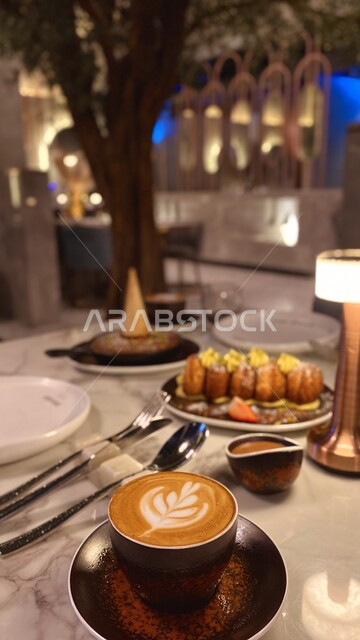  وصفات وأطباق حلويات,  كوب من القهوة برغوة كثيفة مع رسومات مع طبق من الحلويات اللذيذة، مشروب الكابتشينو الساخن, مطاعم وكافيهات عربية خليجية في المملكة العربية السعودية.