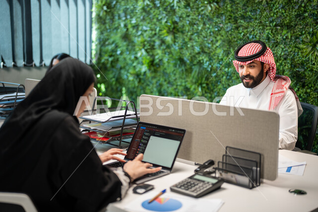 موظفة تقوم بالتواصل مع العملاء من خلال الحاسوب المحمول، فريق عمل عربي سعودي خليجي في مقر الشركة، إنجاز مهام العمل اليومية، مناقشة ومتابعة الاعمال، ايماءات وجه تدل على السعادة, مهن و وظائف سعودية مكتبية.