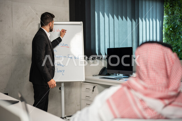Workshop and training, work development and problem solving, discussion and distribution of work tasks, meeting of Saudi Gulf Arab co-workers at the workplace, a businessman wearing a formal suit, the Saudi work environment, unity and teamwork, achieving 