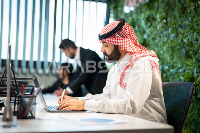 تدوين و تسجيل النتائج و الملاحظات, موظف عربي سعودي خليجي يرتدي الشماغ و الثوب السعودي التقليدي يقوم بإنجاز المهام اليومية، دمج الأعمال مع التقنية و التكنولوجيا, تحقيق أهداف الشركة، التفاهم و التعاون بين الموظفين, بيئة العمل السعودي.