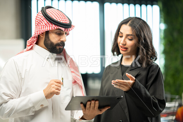 الوحدة والعمل الجماعي لتطوير العمل وحل المشكلات، اجتماع رجل وسيدة أعمال عربيان سعوديان خليجيان في مقر الشركة، مناقشة مهام العمل باستخدام التابليت، بيئة العمل السعودي، تحقيق اهداف الشركة، مهن ووظائف سعودية، خلفية مكتبية.