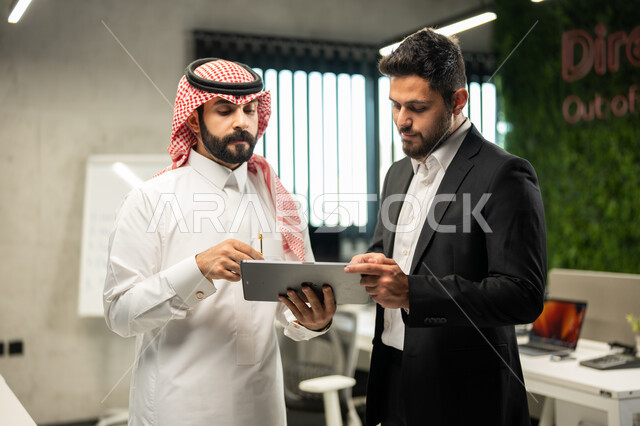 The Saudi work environment, unity and teamwork to develop work and solve problems, two Saudi Arabian Gulf businessmen inside the company's headquarters discussing work tasks, cooperation to achieve the company's goals, Saudi professions and jobs, office b
