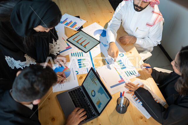 دمج التكنولوجيا و التقنية مع العمل, بيانات إنجاز وتحقيق اهداف الشركه,صورة علوية عامودية لاجتماع فريق عمل عربي خليجي سعودي, جمع بيانات البورصه وسوق الأسهم, دراسة و تحليل الاحصائيات و الرسوم البيانية, إقامة ورشات تعليمية في مقر الشركة، التعاون بين الفريق.