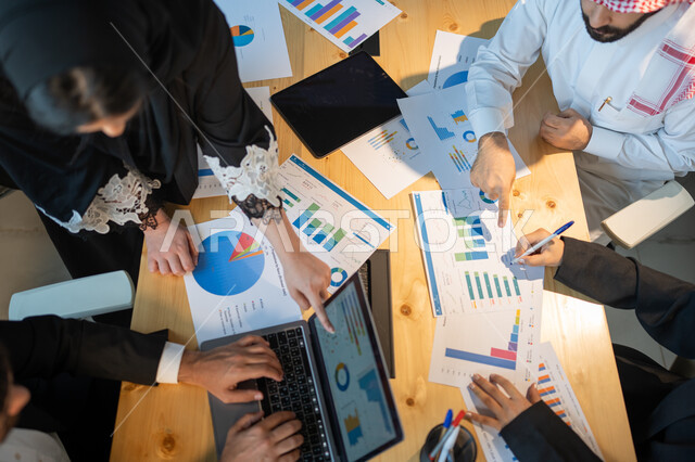 بيانات الاعمال التجاريه، دمج التكنولوجيا و التقنية مع العمل, صورة علوية عامودية لاجتماع فريق عمل عربي خليجي سعودي, جمع بيانات البورصه وسوق الأسهم, دراسة و تحليل الاحصائيات و الرسوم البيانية, إقامة ورشات تعليمية في مقر الشركة، التعاون و التفاهم بين الفريق.