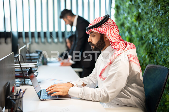 التعاون لتطوير العمل، مهن ووظائف سعودية، تدوين و تسجيل النتائج و الملاحظات, موظف عربي سعودي خليجي يرتدي الشماغ و الثوب السعودي التقليدي يقوم بإنجاز مهام العمل اليومية، دمج الأعمال مع التقنية و التكنولوجيا, تحقيق أهداف الشركة.