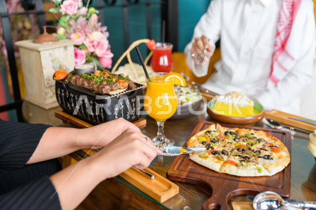 صورة مقربة لمائدة طعام خاصة بزوجين عربيين خليجيين سعوديين ، يجلسان على مائدة الطعام و يتناولان الطعام في المطعم ، قضاء اجواء رائعة  في المطعم ، تشكيلة متنوعة من أصناف الطعام و الماكولات الشهية على الطاولة ، جلسات فريدة و مميزة ، مطاعم و كافيهات في السعودي