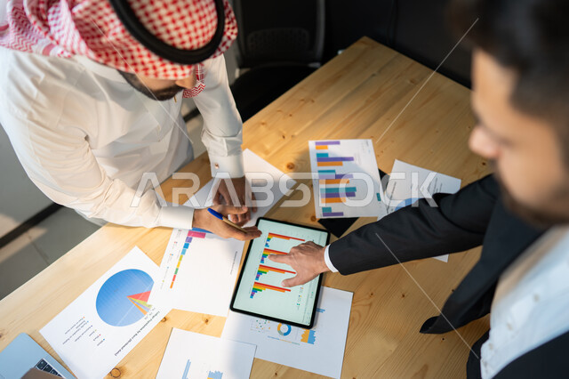 Data of achievement and achievement of the company's goals, a close-up vertical image of a meeting of Saudi Arabian Gulf businessmen inside the company's headquarters, the concept of collaborative management, collecting stock market and stock market data,