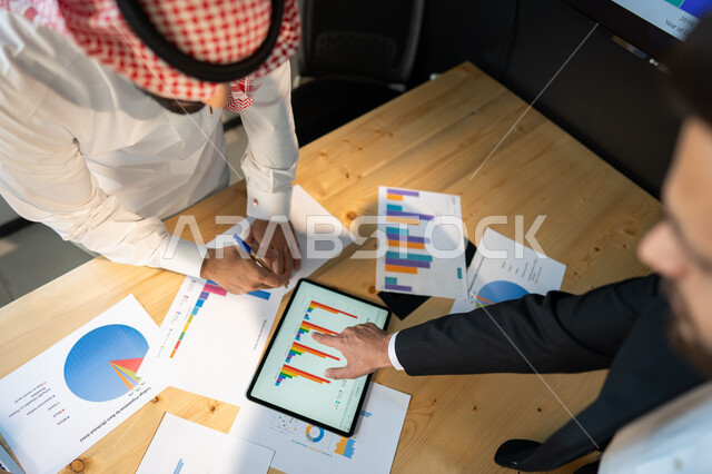 بيانات إنجاز وتحقيق اهداف الشركة، صورة علوية عامودية مقربة لاجتماع رجال أعمال عربيين سعوديين خليجيين داخل مقر الشركة، مفهوم الإدارة المتعاونة، جمع بيانات البورصه وسوق الأسهم, دراسة و تحليل الاحصائيات و الرسوم البيانية, دمج التكنولوجيا مع العمل.