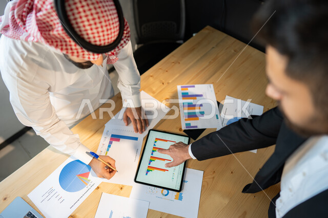 تحقيق الاهداف المالية للشركة، صورة علوية عامودية مقربة لاجتماع رجال فريق عمل عربي خليجي سعودي، مفهوم الإدارة المتعاونة، جمع بيانات البورصه وسوق الأسهم, دراسة و تحليل الاحصائيات و الرسوم البيانية, دمج التكنولوجيا مع العمل.