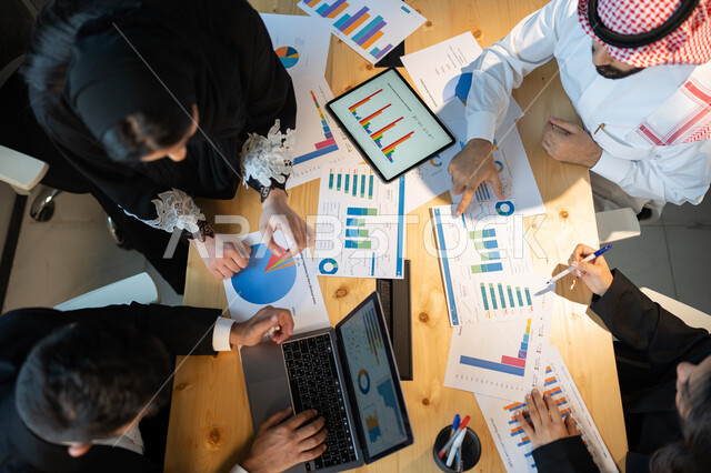 Business data, integrating technology and technology with work, a vertical overhead image of an Arab-Gulf-Saudi business team meeting, stock market and stock market data collection, studying and analyzing statistics and graphs, holding educational worksho