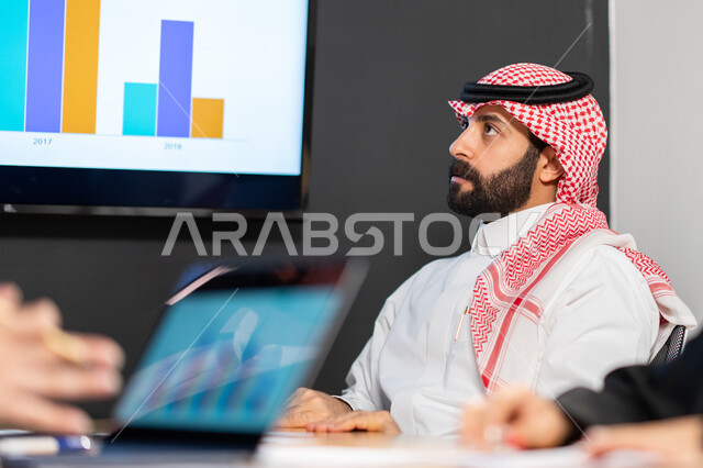 ايماءات وجه تدل على التركيز و الاندماج, صورة مقربة لموظف عربي خليجي سعودي في ورشة تعليمية ضمن مقر الشركة,  قسم البيانات و الإحصائيات, استخدام الحاسب المحمول في الأعمال والحسابات, دمج التقنية و التكنولوجيا مع البيئة العملية, العمل في روح الفريق.