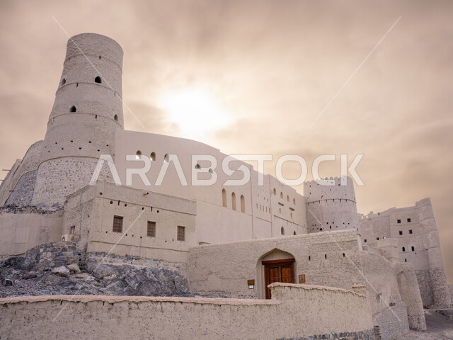 معلم عسكري تاريخي اثري ،موقع استراتيجي هام, منظر السماء الملبدة بالغيوم, قلعة بهلاء عبري مبنية من الطين في سلطنة عمان ,التصميم والفن الهندسي المعماري بالطراز الهندسي القديم،  معالم سياحيه تراثيه مشهورة .