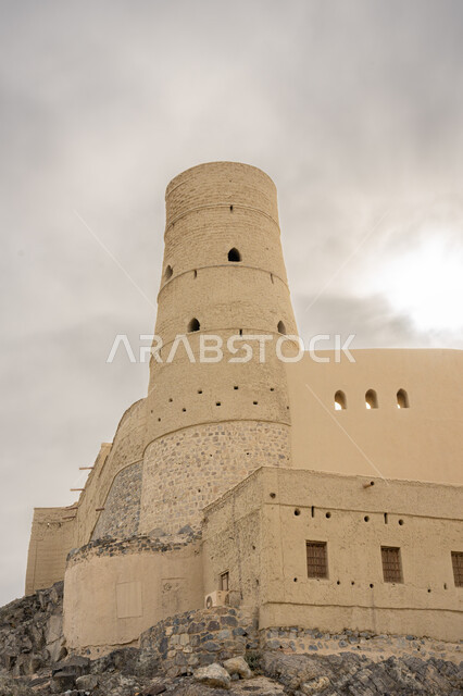 معالم سياحيه تراثيه مشهورة, موقع استراتيجي هام, منظر السماء الملبدة بالغيوم, قلعة بهلاء عبري مبنية من الطين في سلطنة عمان , معلم عسكري تاريخي اثري ،التصميم والفن الهندسي المعماري بالطراز الهندسي القديم .