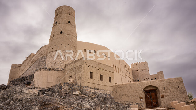 منظر السماء الملبدة بالغيوم, قلعة بهلاء عبري مبنية من الطين في سلطنة عمان , معلم عسكري تاريخي اثري ،التصميم والفن الهندسي المعماري بالطراز الهندسي القديم،  معالم سياحيه تراثيه مشهورة, موقع استراتيجي هام .