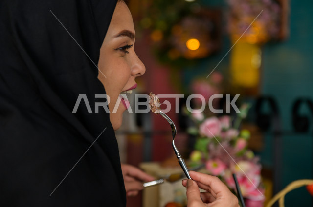 A close-up of a Saudi Arabian Gulf woman eating in the restaurant, spending a wonderful atmosphere in the restaurant, many types of food and dishes on the table, unique and distinctive sessions, restaurants and cafes in Saudi Arabia