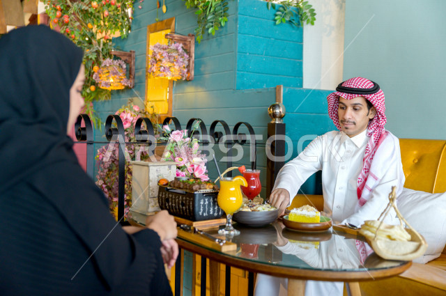 زوجان عربيان خليجيان سعوديان يجلسان على مائدة الطعام و يتناولان الطعام في المطعم ، قضاء اجواء رائعة  في المطعم ، تشكيلة متنوعة من أصناف الطعام و الماكولات الشهية على الطاولة ، جلسات فريدة و مميزة ، مطاعم و كافيهات في السعودية