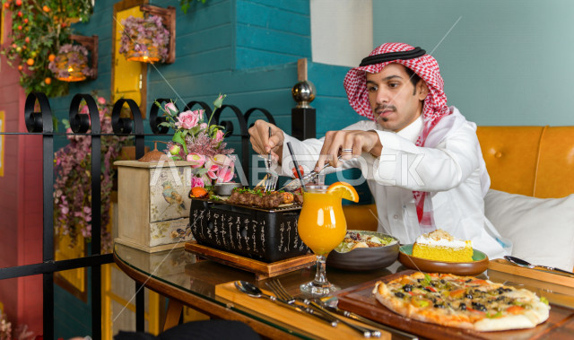 صورة مقربة لرجل عربي خليجي سعودي يجلس على مائدة الطعام و يقوم بتناول الطعام في المطعم ، قضاء اجواء رائعة  في المطعم ، تشكيلة متنوعة من أصناف الطعام و الماكولات الشهية على الطاولة ، جلسات فريدة و مميزة ، مطاعم و كافيهات في السعودية