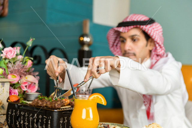 صورة مقربة لرجل عربي خليجي سعودي يجلس على مائدة الطعام و يقوم بتناول الطعام في المطعم ، قضاء اجواء رائعة  في المطعم ، تشكيلة متنوعة من أصناف الطعام و الماكولات الشهية على الطاولة ، جلسات فريدة و مميزة ، مطاعم و كافيهات في السعودية