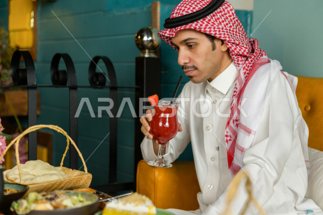 صورة مقربة لرجل عربي خليجي سعودي يجلس على مائدة الطعام ويشرب مشروب الفراولة في المطعم ، قضاء اجواء رائعة  في المطعم ، جلسات فريدة و مميزة ، مطاعم و كافيهات في السعودية