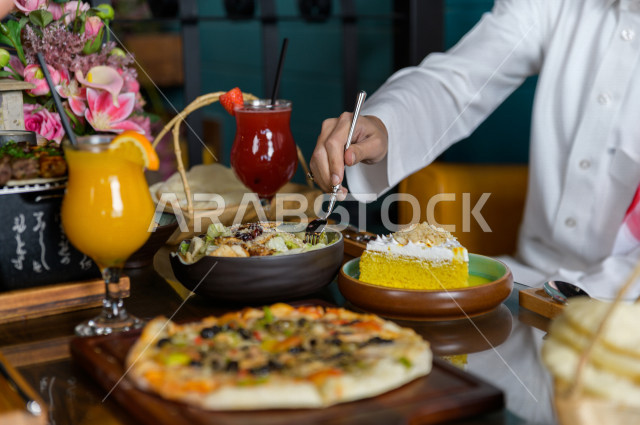 صورة مقربة لرجل عربي خليجي سعودي يجلس على مائدة الطعام و يقوم بتناول الطعام في المطعم ، قضاء اجواء رائعة  في المطعم ، تشكيلة متنوعة من أصناف الطعام و الماكولات الشهية على الطاولة ، جلسات فريدة و مميزة ، مطاعم و كافيهات في السعودية