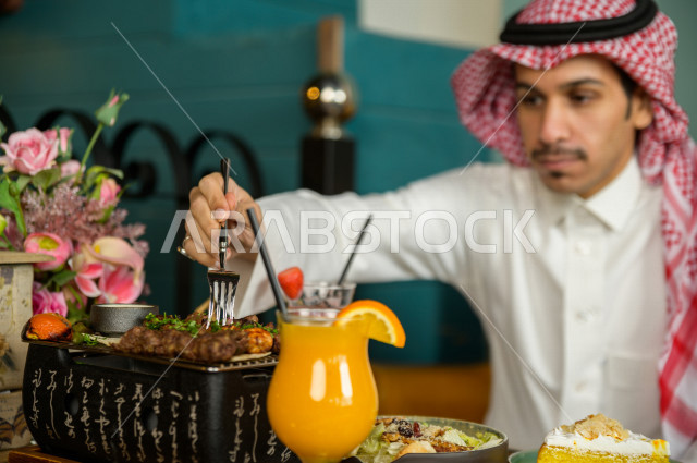 صورة مقربة لرجل عربي خليجي سعودي يجلس على مائدة الطعام و يقوم بتناول الطعام في المطعم ، قضاء اجواء رائعة  في المطعم ، تشكيلة متنوعة من أصناف الطعام و الماكولات الشهية على الطاولة ، جلسات فريدة و مميزة ، مطاعم و كافيهات في السعودية