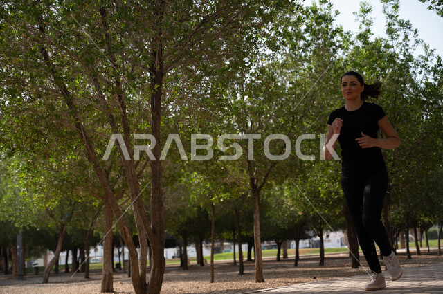  ممارسة النشاط البدني في الهواء الطلق، الصحة واللياقة البدنية و الجسدية، فتاة عربية خليجية سعودية تقوم برياضة الجري للحفاظ على الرشاقة، التنزه في إحدى الحدائق العامة في المملكة العربية السعودية, صورة الجسم بالطول الكامل.