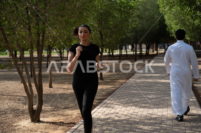 A Saudi Gulf Arab girl does jogging to keep fit, a Saudi Gulf Arab man walks in the park corridor, health and physical fitness, outdoor physical activity, hiking in a public park in the Kingdom of Saudi Arabia.
