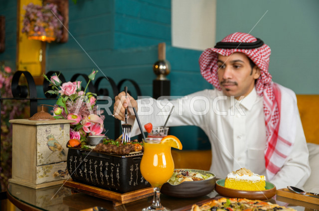 صورة مقربة لرجل عربي خليجي سعودي يجلس على مائدة الطعام و يقوم بتناول الطعام في المطعم ، قضاء اجواء رائعة  في المطعم ، تشكيلة متنوعة من أصناف الطعام و الماكولات الشهية على الطاولة ، جلسات فريدة و مميزة ، مطاعم و كافيهات في السعودية