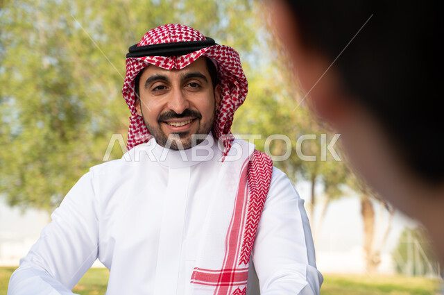قضاء أوقات ممتعة في الحدائق الخضراء, نزهه في الطبيعة و الهواء الطلق, صورة مقربة لرجل عربي خليجي سعودي مبتسم  ينظر إلى الكاميرا , إيماءات وجه تدل على السعادة و السرور , خلفية الطبيعة.