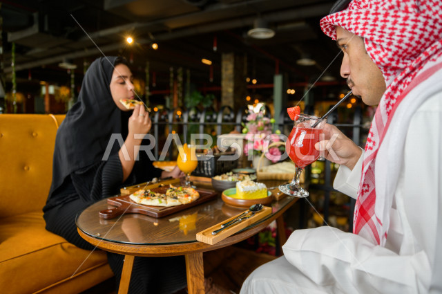 زوجان عربيان خليجيان سعوديان يجلسان على مائدة الطعام و يتناولان الطعام في المطعم ، قضاء اجواء رائعة  في المطعم ، تشكيلة متنوعة من أصناف الطعام و الماكولات الشهية على الطاولة ، جلسات فريدة و مميزة ، مطاعم و كافيهات في السعودية