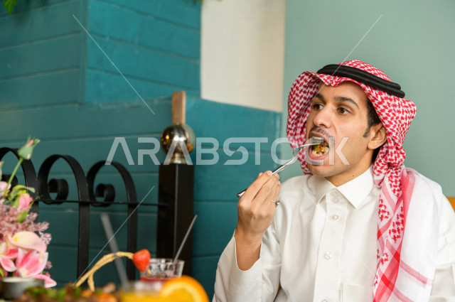 صورة مقربة لرجل عربي خليجي سعودي يجلس على مائدة الطعام و يقوم بتناول الطعام في المطعم ، قضاء اجواء رائعة  في المطعم ، تشكيلة متنوعة من أصناف الطعام و الماكولات الشهية على الطاولة ، جلسات فريدة و مميزة ، مطاعم و كافيهات في السعودية