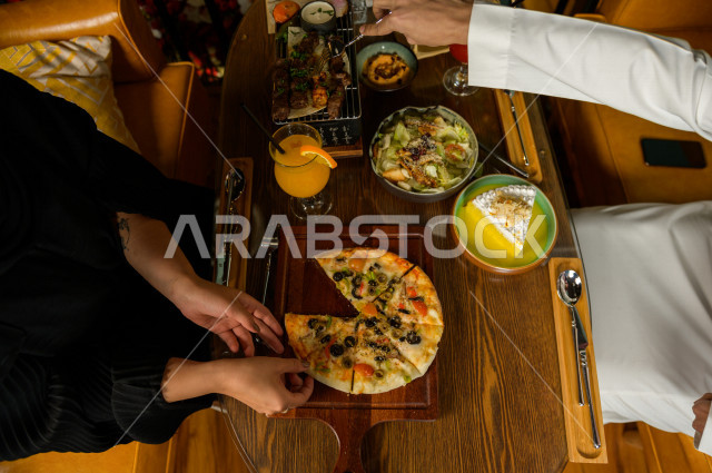A picture from above of a dining table for a Saudi Arabian Gulf couple, sitting at the dining table and eating in the restaurant, spending a wonderful atmosphere in the restaurant, a variety of food items and delicious food on the table, unique and distin