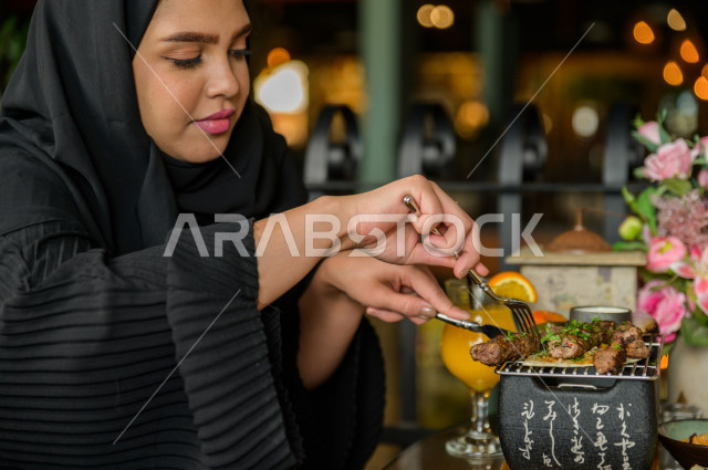 A close-up of a Saudi Arabian Gulf woman eating in the restaurant, spending a wonderful atmosphere in the restaurant, many types of food and dishes on the table, unique and distinctive sessions, restaurants and cafes in Saudi Arabia