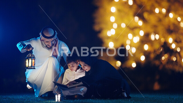 تحفيظ القرآن للابناء في شهر رمضان المبارك، عائلة عربية خليجية سعودية في الحديقة العامة للمنزل، أب عربي سعودي يحمل بيده فانوس رمضان، إضاءة وزينة شهر رمضان، مناسبات دينية اسلامية، قضاء أوقات ممتعه مع العائله