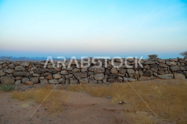 جدار مبني من الحجر و الصخور الطبيعية في الصحراء، الأجواء الصيفية في البيئة الصحراوية في المملكة العربية السعودية، نمو الأعشاب و النباتات الصحراويه في البراري، خلفية الطبيعة.