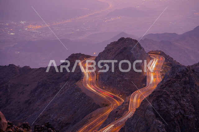 ممر جبلي ملتوي خطير في طريق الهدا مع مسارات ضوئية ,صورة جوية لمنطقة عقبة الهدا في مدينة الطائف في المملكة العربية السعودية وقت غروب الشمس، حركة مرور السيارات في الشوارع ، أماكن سياحية مشهورة، القمم والمرتفعات الجبلية