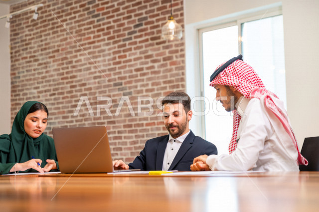 اجتماع اداري مع مجموعة من الأشخاص السعوديين الخليجيين في غرفة الاجتماعات  ، اجتماع رجال اعمال و سيده اعمال سويا داخل الشركة ، استخدام الكمبيوتر المحمول لادارة الاعمال ،  شركة سعودية ، عمل خليجي ،  فريق العمل 