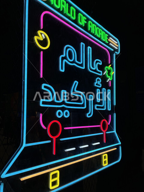 اللعب في صالات الألعاب الألكترونية في موسم الجيمرز ٨ في بوليفارد الرياض، صورة من الجانب للوحة إعلانية بارزة، نيون مضيء لكلمة عالم الأركيد، قضاء أوقات ممتعة في ممارسة الأنشطة الترفيهية، التحدي والمنافسة بين اللاعبين السعوديين الخليجيين