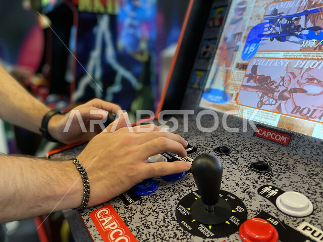 اللعب في صالات الألعاب الإلكترونية في موسم الجيمرز ٨ في بوليفارد الرياض، صورة مقربة لأيدي شاب يقوم باللعب بألعاب الأركيد المسلية، قضاء أوقات ممتعة في ممارسة الأنشطة الترفيهية، اللعب والتحدي في قسم التحديات (تشالينج زون)، فعاليات جذب السياح للسعودية.