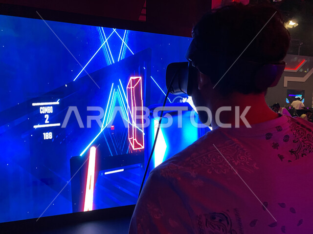  شاب عربي خليجي سعودي يرتدي نظارة الواقع لاافتراضي يلعب في لعبة (بيت سايبير) ثلاثية الابعاد في منطقة التحديات (تشالينج زون) في موسم الجيمرز 8 في بوليفارد الرياض, ألعاب إلكترونيه تفاعليه ثري دي متطوره, محاكاة العالم الافتراضي، أنشطة ترفيهية سياحية.